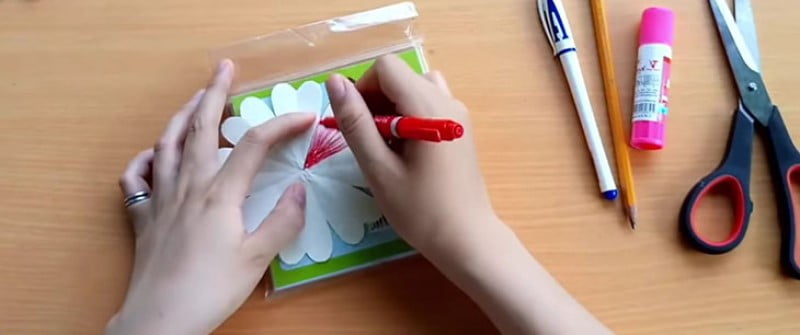 Bước 1: Dùng các mẫu giấy trắng hình vuông đã chuẩn bị, cắt thành hình hoa và trang trí bằng cách lấy bút mực đỏ tô cánh hoa.
